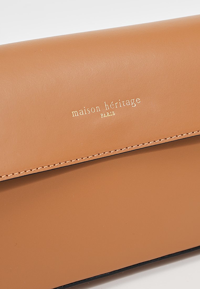 Tasche aus braunem Leder mit strukturiertem Finish, ausgestattet mit einem goldenen eingeprägten Logo und einem klaren, minimalistischen Design. Kanten in einem dunkleren Farbton genäht.