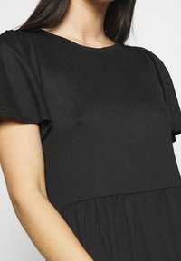 Robe noire avec une partie supérieure texturée, manches courtes et une partie inférieure froncée, offrant une coupe ample et décontractée.