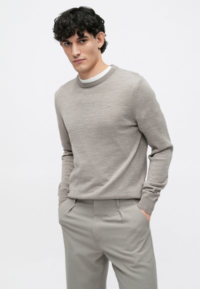 Suéter de malha cinza claro com decote redondo, usado sobre uma camisa branca. Combinado com calças plissadas cinza claro, exibindo uma textura suave.