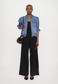Blå satengkort jakke med puffede ærmer, parret med en sort jumpsuit, og suppleret med en mørk håndtaske og sorte spidse sko.