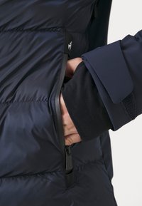 Námořnická puffer bunda s boční kapsou a černým zipem, hladkou texturou a přiléhavým manžetovým uzávěrem na suchý zip.