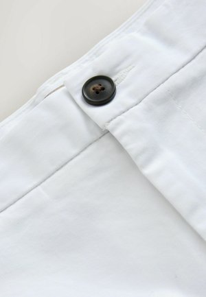 Nahaufnahme eines weißen Stoffes mit einem dunkelbraunen Vierlochknopf, der nahe einer genähten Knopflöchern befestigt ist.