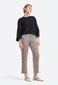Czarny krótki sweatshirt, wzorzyste beżowe spodnie w panterkę i jasne buty. Stylizacja ma luźny krój i szerokie rękawy.