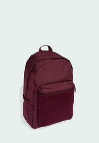 Mochila marrón con un exterior texturizado, compartimento principal grande, bolsillo frontal con cremallera y asa de bucle. Presenta un detalle de marca minimalista.