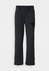 Black sweatpants with a wide-leg design, elastic waistband, drawstring, and a glossy black patch featuring “HUGO” on the left thigh.