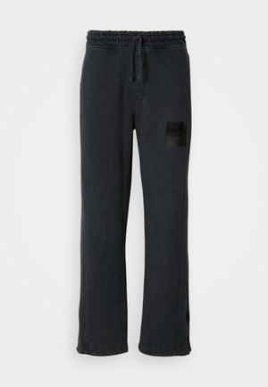 Black sweatpants with a wide-leg design, elastic waistband, drawstring, and a glossy black patch featuring “HUGO” on the left thigh.