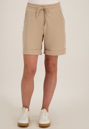 Beige knielange shorts met opgerolde boorden, een elastische tailleband met trekkoord, gedragen met witte sneakers met rubberen zolen.
