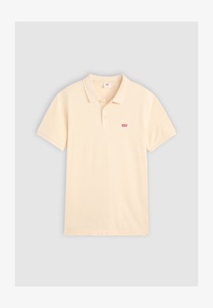 Polo tričko v svetlej krémovej farbe, vyrobené z jemnej bavlny, s klasickým golierom, krátkymi rukávmi a malým červeným logom Levi's na ľavej hrudi.