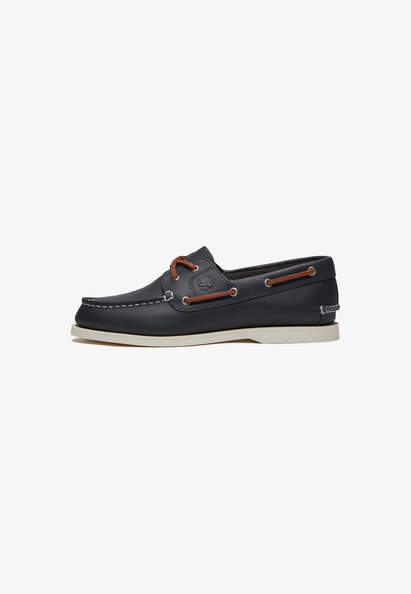 Scarpe da barca in pelle blu navy con lacci e occhielli marroni, suola in gomma bianca e dettagli cuciti lungo il bordo superiore.