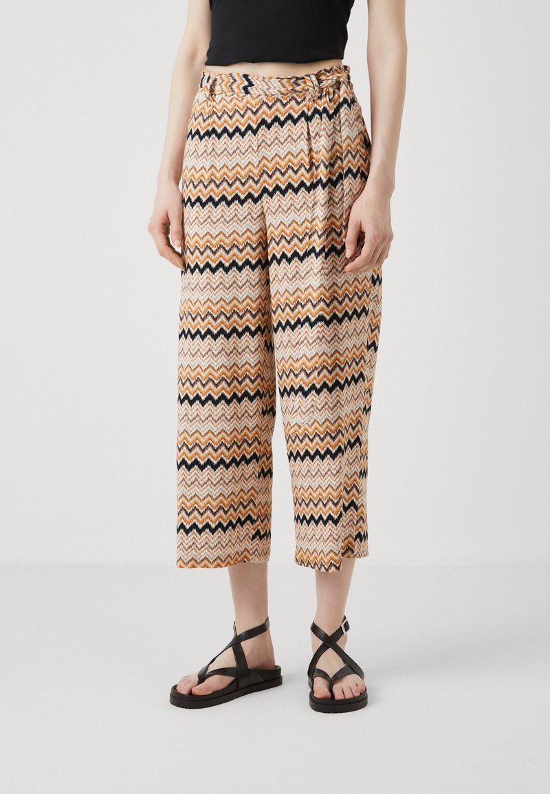 Pantalons larges et cropped avec un motif chevron ondulé dans les couleurs orange, noir et crème ; tissu léger avec un détail de taille nouée.