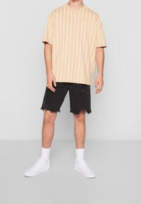 Vaaleanbeige raidallinen t-paita lyhyillä hihoilla, yhdistetty mustiin kuluneisiin denim-shortsit. Täydennetty valkoisilla tennareilla ja nilkkasukilla.