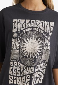 Sort bomulds t-shirt med hvid retro grafikdesign med solmotiver og stiliseret tekst. Rund halsudskæring, afslappet pasform og korte ærmer.