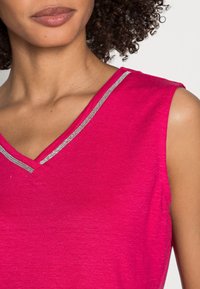 Rosa ärmelloses Oberteil mit V-Ausschnitt, versehen mit einem silbernen Besatz entlang des Ausschnitts. Weicher Stoff, lässiges Design, geeignet für warmes Wetter.
