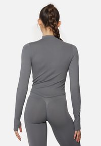 Long-sleeved athletic top in gray, made of smooth, stretchy fabric. Features a fitted design with a high neckline and subtle seams.