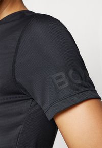 Camisola atlética preta com tecido texturizado, mangas curtas e costura visível. Apresenta um logótipo "BOSS" impresso no braço.