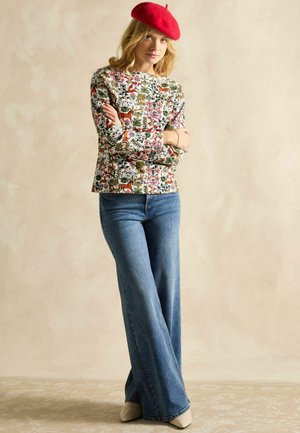 Floral long-sleeve top with a cream background, paired with high-waisted flared blue jeans and light-colored heeled shoes; red beret accent.