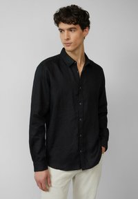Chemise noire à manches longues en tissu léger, avec un plastron boutonné et un col, offrant une coupe décontractée et peu de détails.