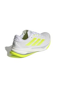 White athletic shoe with neon yellow accents, textured upper, flat laces, and a cushioned sole featuring a contrasting yellow and gray design.