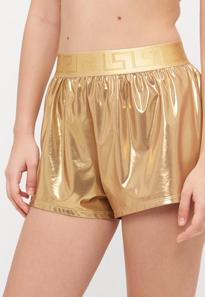 Shorts dorés, métalliques et brillants avec une taille élastique arborant un motif grec. Texture lisse, longueur mi-cuisse et coupe décontractée.
