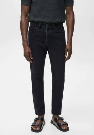 Jeans de mezclilla negros con corte recto, costura sutil en los bolsillos delanteros y una textura suave, combinados con sandalias negras.