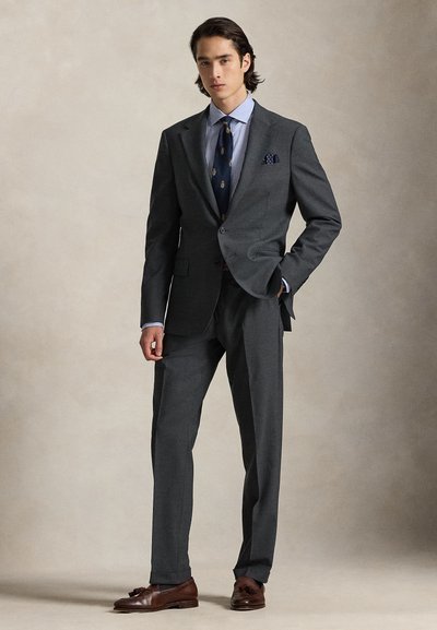Γκρι κοστούμι με ραμμένο γιακά notch, σε συνδυασμό με μπλε ριγέ πουκάμισο και ναυτικό μπλε γραβάτα. Καφέ δερμάτινα παπούτσια ολοκληρώνουν το σύνολο.