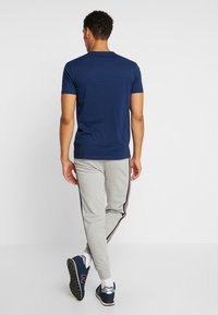 Mørkeblå kortærmet skjorte kombineret med lysegrå joggingbukser med sidelister. Bruges med mørke atletiske sko og hvide sokker.