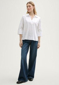 Blouse blanche à col avec des manches trois quarts, associée à un jean en denim bleu évasé. Design simple, tissu léger et coupe décontractée.