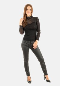 Blusa negra de manga larga con tejido de malla transparente y escote de cuentas, combinada con pantalones de piel ajustados negros y zapatos de tacón.