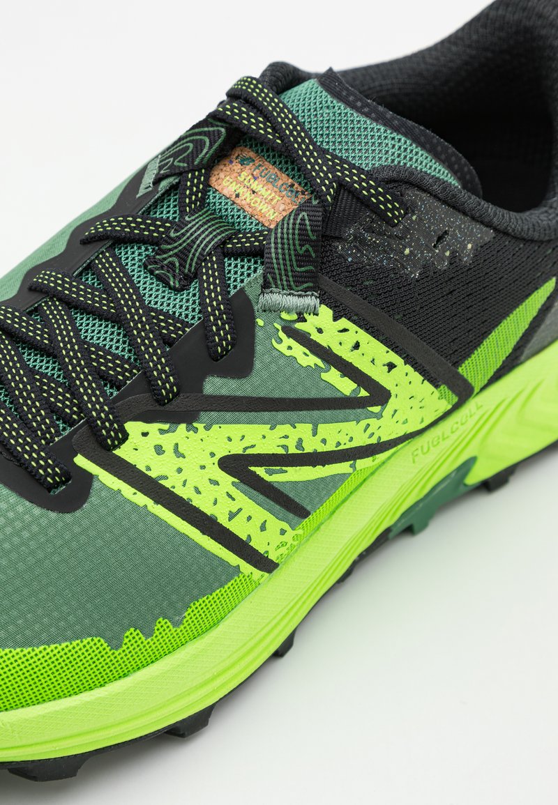 Zapatilla deportiva verde y negra con parte superior de malla, acentos amarillos llamativos, material texturizado y un diseño de suela robusta para tracción.