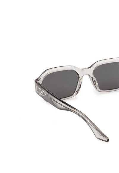 Gafas de sol con montura de plástico gris transparente, lentes rectangulares oscuras y patillas ligeramente curvadas, mostradas sobre fondo blanco.