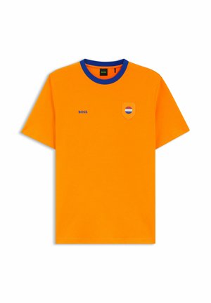 Jasnopomarańczowa koszulka z krótkim rękawem i niebieskim okrągłym kołnierzem, z małym napisem "BOSS" na lewej piersi oraz naszywką w kształcie tarczy z czerwonymi, białymi i niebieskimi paskami.