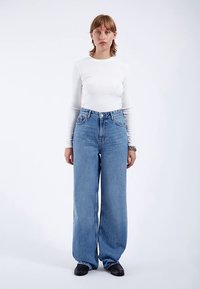 Camiseta blanca de manga larga y ligera combinada con jeans de mezclilla azul de tiro alto y pierna ancha. Textura suave con un diseño clásico de cinco bolsillos.