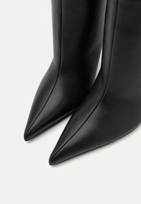 Schwarze kniehohe Lederstiefel mit spitzem Schuhkopf und glatter Textur, die sich durch klare Linien und minimale Nähten auszeichnen.