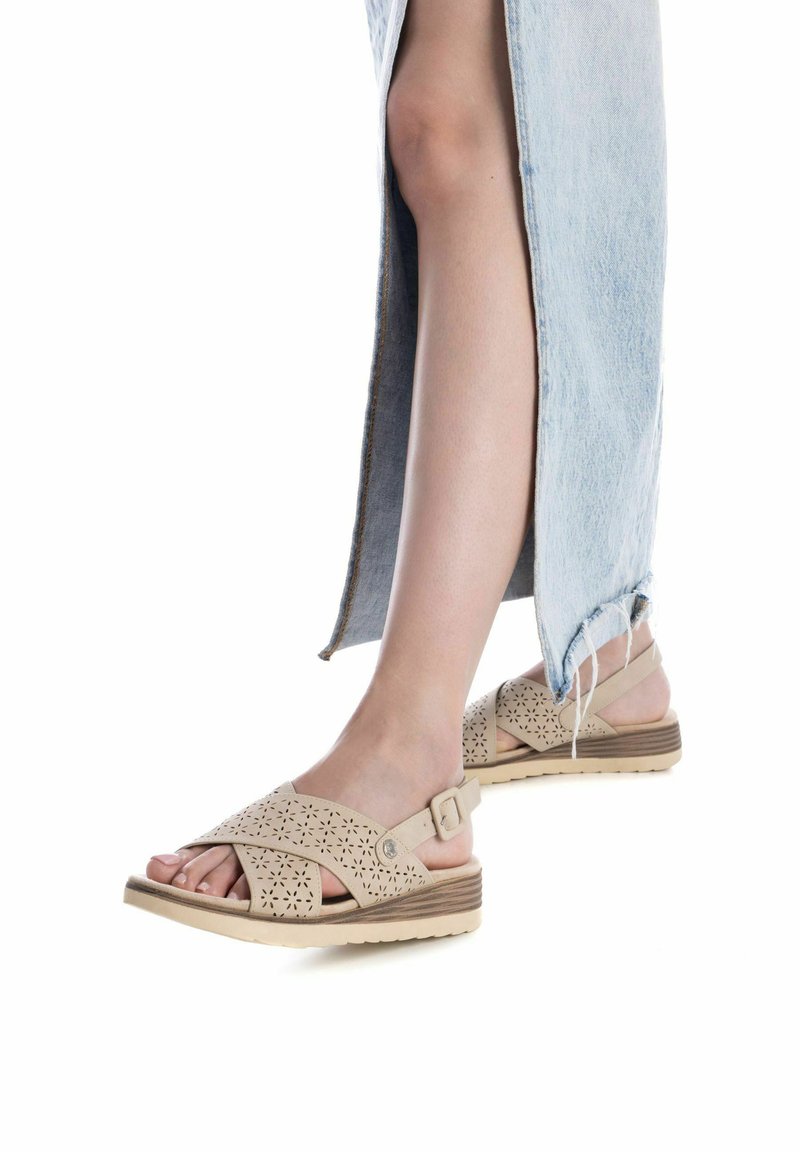 Sandalias beige perforadas con diseño de tiras cruzadas, hebilla ajustable y suela texturizada. Combinadas con una falda de mezclilla clara.
