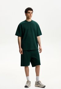 Zeleni bombažni oversized majica, kombinirana s usklade šortsi. Ima sproščen kroj, okroglo izrez in vidne šive.