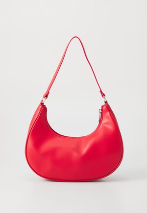 Sac à épaule rouge en forme de croissant avec une texture lisse et une fine bandoulière sur un fond clair uni.