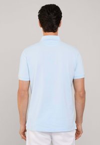 Polo shirt bleu clair à manches courtes avec un col classique et une texture lisse ; il présente un ourlet droit et des détails de couture subtils à l'arrière.