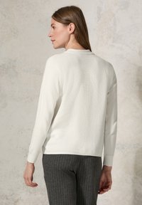 Haut texturé blanc à manches longues avec un col rond, associé à un pantalon gris à rayures. Le tissu a un aspect côtelé.