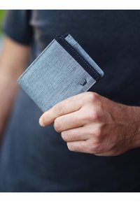 Gray fabric wallet held in hand, featuring a black accent, slim design, and visible stitching, with a small logo in the corner.