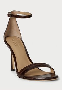 Sandalo stiletto in ecopelle marrone con motivo coccodrillo, punta aperta, cinturino alla caviglia con fibbia e tacco affusolato. Soletta beige liscia.