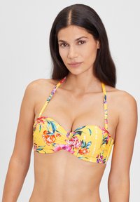 Geel bikini top met bloemenpatroon, voorgevormde cups en dunne verstelbare bandjes. Heeft een gedraaide voorkant en levendige kleuren.