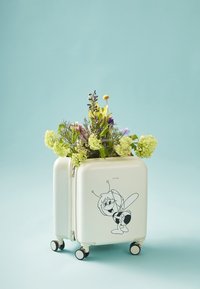 Valise rigide blanche avec un design de petite abeille noire en cartoon, remplie de fleurs colorées variées, reposant sur quatre petites roues.