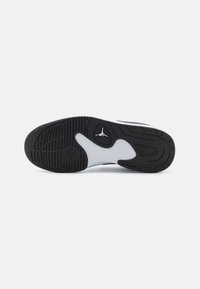 Semelle de basket noire et blanche avec des motifs de bande de roulement, un détail circulaire près des orteils, et un logo ressemblant à une silhouette sautant au centre.