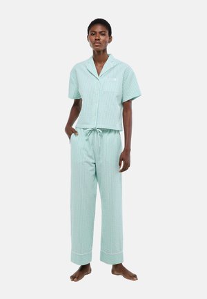 Femme debout pieds nus portant un haut à manches courtes boutonné à rayures vertes et blanches et un pantalon ample assorti avec cordon de serrage, pyjama.