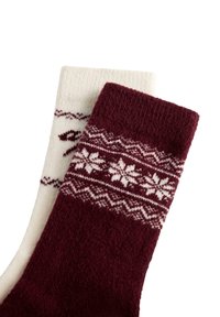 Para skarpetek na drutach z zimowymi wzorami; jedna bordowa z białymi śnieżynkami, druga kremowa z bordowym wzorem na białym tle.