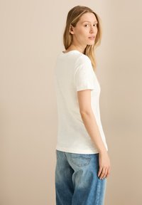 Witte korte mouwen t-shirt van zachte stof, met een ronde halslijn. Draag het met lichte blauwe denim jeans, ontspannen pasvorm, licht vervaagd.