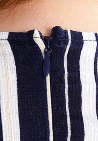 Primo piano di un tessuto a righe blu navy e bianco con una cerniera blu navy parzialmente zipata su uno sfondo di pelle.