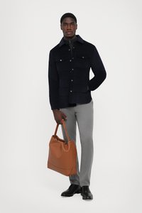 Marineblaues Cordjackett mit vorderen Taschen, graue Hose und eine braune Ledertasche. Schwarze Schuhe vervollständigen das Outfit.