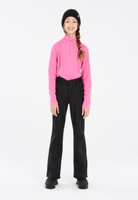 Pull en polaire rose avec un col zippé quart, associé à un pantalon extérieur à motif pied-de-poule noir et un bonnet en tricot noir.