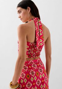 Top rosa brillante con scollatura a halter caratterizzato da motivi floreali, schiena arricciata e chiusura con lacci. Abbinato a una gonna coordinata, che presenta disegni vibranti simili.